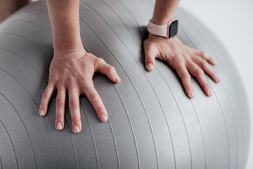 Close-up of two hands pressing down on a large gray exercise ball