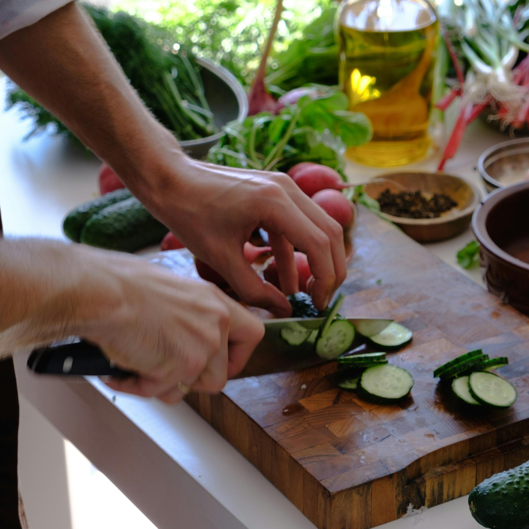 A person slicing fresh cucumbers on a wooden cutting board