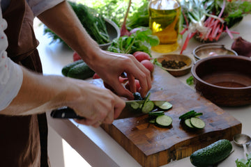 A person slicing fresh cucumbers on a wooden cutting board